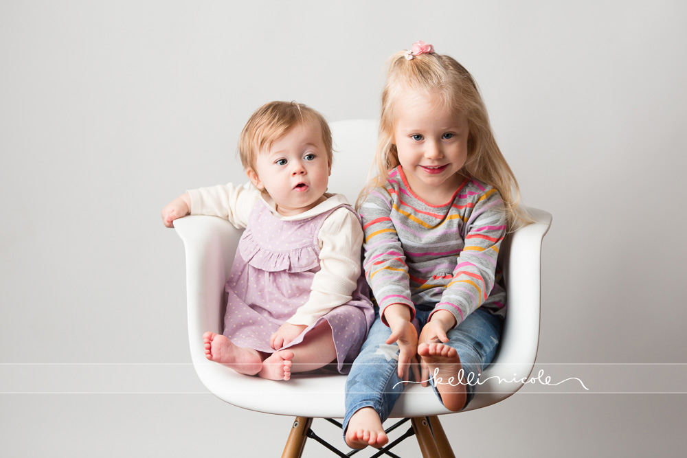 posed, sisters, children, photography, session, photo shoot, houston, texas, kelli nicole photography, baby girl, color, baby photography, houston baby photographer, studio, baby girl, child posing, baby photography tutorial, studio baby lighting, paul c buff einstein lighting, family, houston family photography, white backdrop, white photography session, white studio, white studio houston, children, siblings, two siblings, white wood, bed, fake bed setup, studio bed setup, lifestyle, candid, eames chair